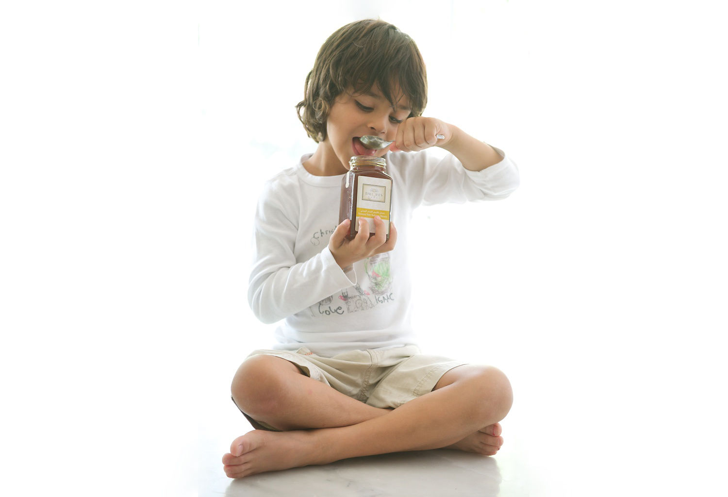 small boy eats raw honey from a jar with spoon
