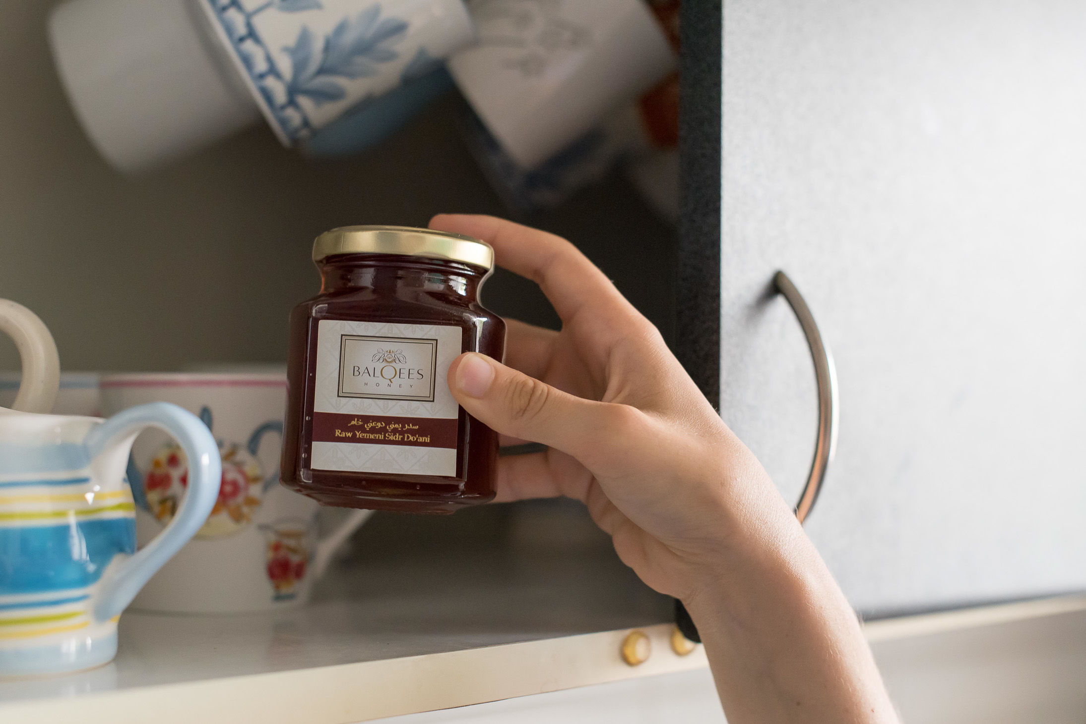 hand putting jar of raw honey into storage cupboard