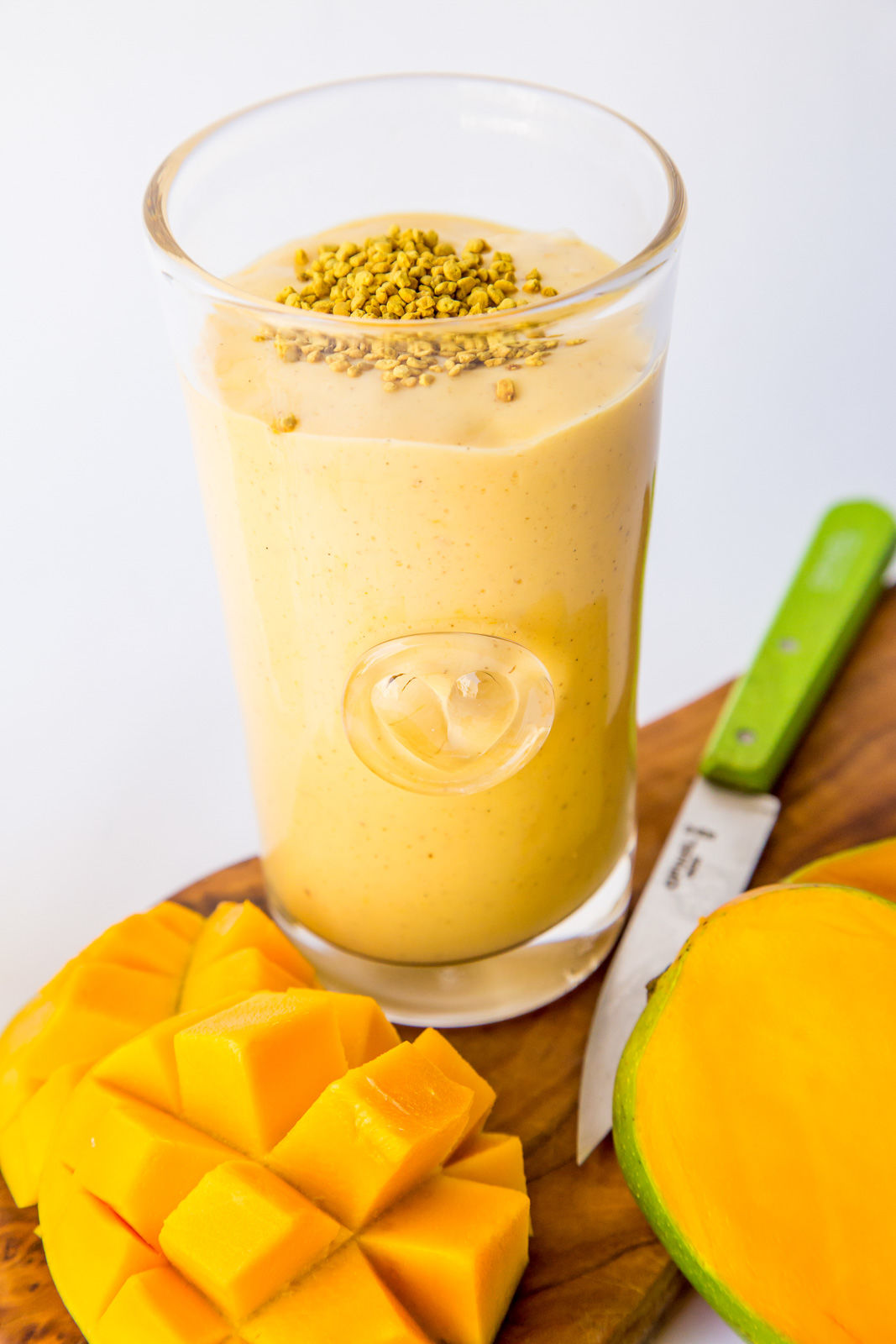 A glass of mango smoothie topped with bee pollen and raw honey