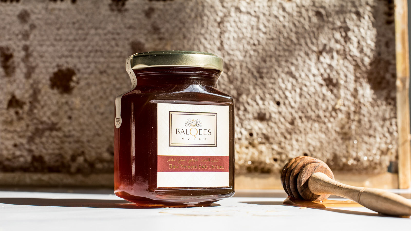 a jar of raw honey, a honey drizzler in front of honeycomb