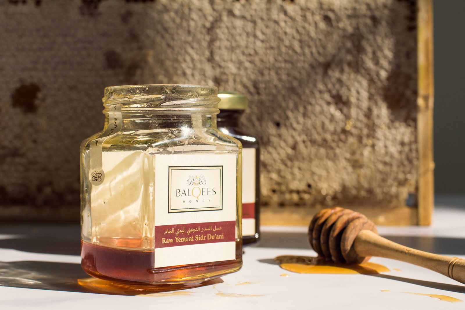 two jars of raw honey in front of a honeycomb