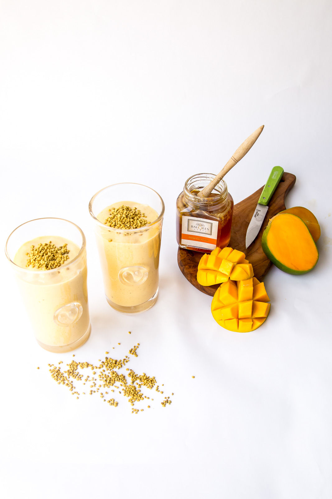 two glasses of mango smoothie and a jar of raw honey