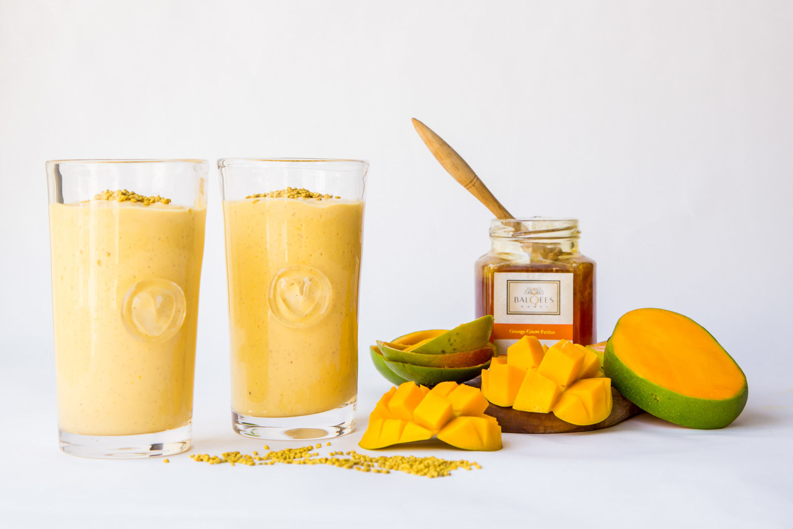 Two glasses of mango smoothie, a jar of honey and some mangoes